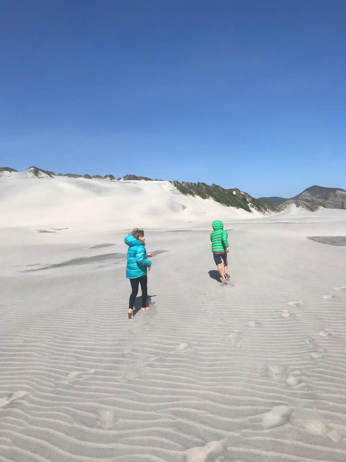 Two children running across sand dunes near Wharariki Beach